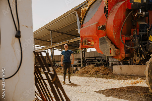Young farmer walking beside large agricultural equipment in a dairy farm. Farming, rural work and agricultural industry concept.