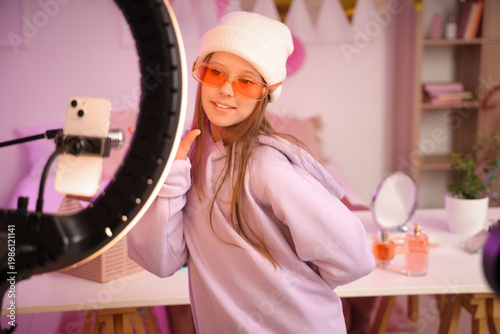 Teenage beauty blogger with sunglasses recording video in bedroom