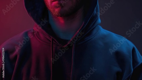 A person wearing a hoodie stands against a bright red light, creating a striking contrast