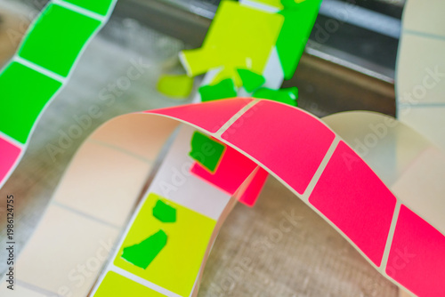 Bright coloured Illuminous adhesive label rolls on an industrial production line in packaging and manufacturing environment. Food labels for health safety and hygiene purposes.