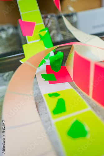 Bright coloured Illuminous adhesive label rolls on an industrial production line in packaging and manufacturing environment. Food labels for health safety and hygiene purposes.