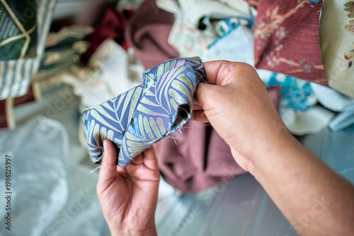 Hands of a Worker sorting mixed fabric offcuts and textile waste from industrial bin for recycling and reuse. Industrial recycling programme aimed to cut costs and be better for the environment.