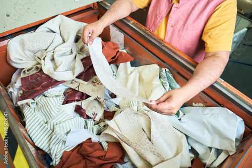 Hands of a Worker sorting mixed fabric offcuts and textile waste from industrial bin for recycling and reuse. Industrial recycling programme aimed to cut costs and be better for the environment.