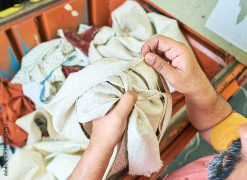 Hands of a Worker sorting mixed fabric offcuts and textile waste from industrial bin for recycling and reuse. Industrial recycling programme aimed to cut costs and be better for the environment.