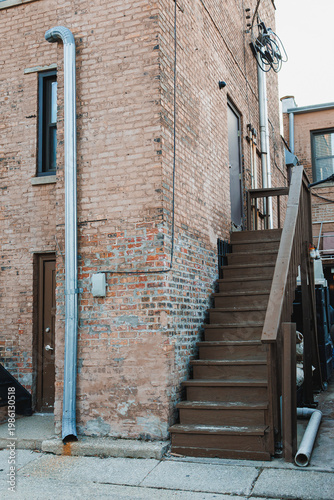 Фотография Stairs lead up to a door on a brick building in an urban area with a metal drain