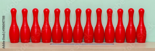 Bild auf Leinwand Thirteen red bowling pins standing in perfect alignment on a wooden surface, a r