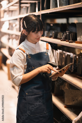 Retail worker in apron using tablet and scanner in store aisle, focused customer service and inventory check