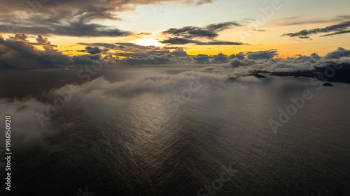Golden ocean with mist and distant islands under a cloudy sky at sunset, calm waters. Seychelles, Mahe.