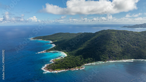 An isolated beach cove framed by lush green hills and vibrant blue sea. La Digue, Seychelles.