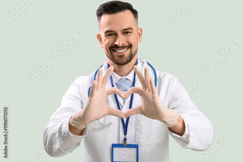 Male doctor making heart with his hands on green background