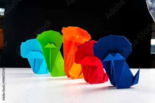 Bright colorful origami paper dogs  on a white surface. Concept of diversity, teamwork, and family represented by colorful paper figures.