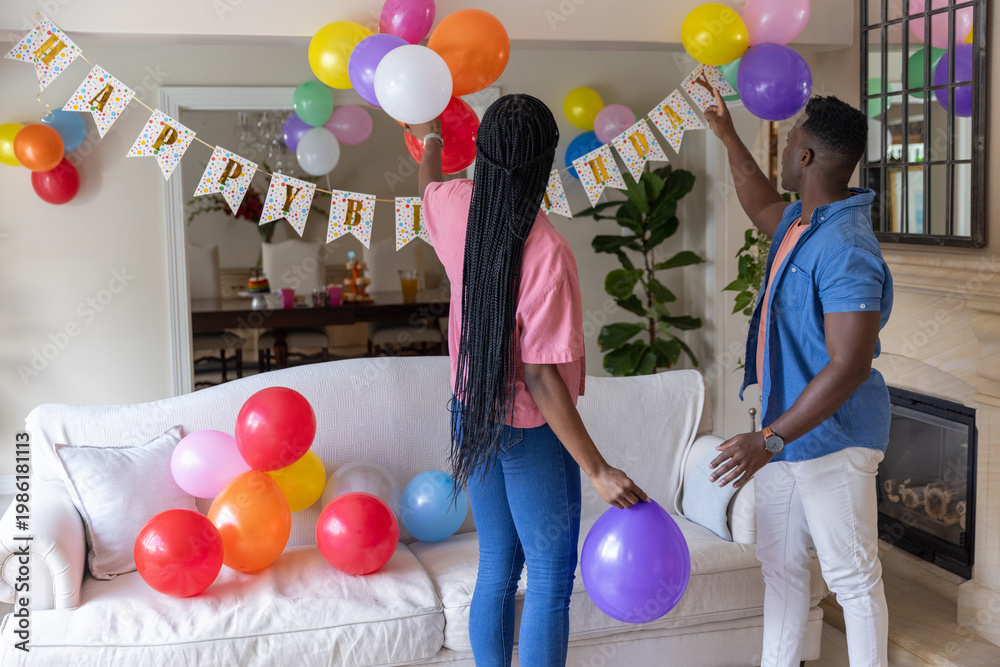 Obraz premium African American couple decorating living room with colorful latex balloons and Birthday banner