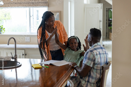African American family helping child with homework at kitchen island using open workbook green pen