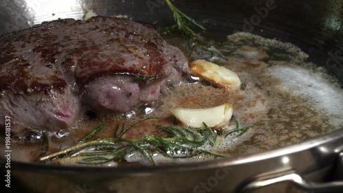 Thick ribeye steak bastes in butter with garlic and rosemary
