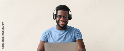 Schilderij op canvas A man sits at a desk working on a laptop while wearing headphones