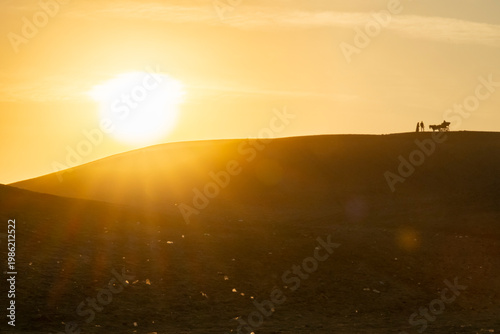 Sunset over hill with people and cart in the distance, highlighting everyday life and work routines