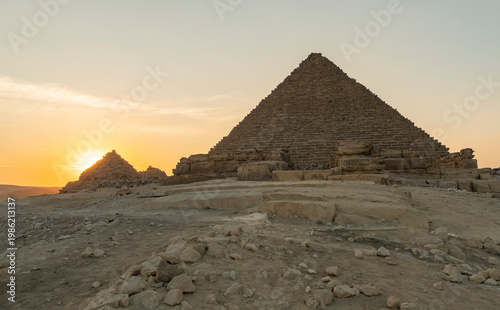 Pyramids at Giza during sunset with clear sky and stones in foreground seen from an angled view