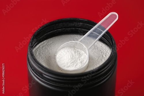 Spoon with creatine proteine in an opened can for sporty lifestyle. Elevated  view isolated on red. 