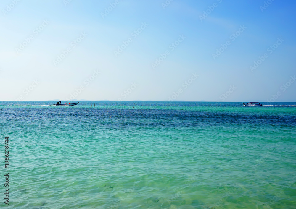 Fototapeta premium Fast motorboat carries tourists across ocean. Boat moves sea on sunny day near coastline in tropical island. Boat travels through clear blue sea water under bright sky. Traveling on sea in Vietnam. 