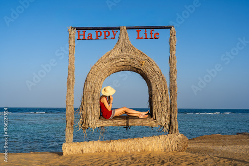 independent woman in hat sitting on bench, enjoying the charms of life in Egyptian resort, with all-inclusive wristband, turquoise sea, and 