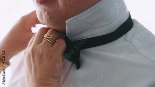 Slow Motion Close-Up Push-In of Groom while older woman's hands fixing his bow tie with Window Lighting