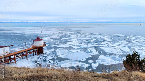 Old Rusty Bridge and House on the Shore of Lake with Breaking Ice