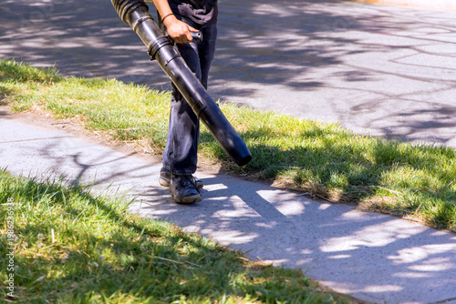 Person uses leaf blower on sidewalk and lawn in residential area
