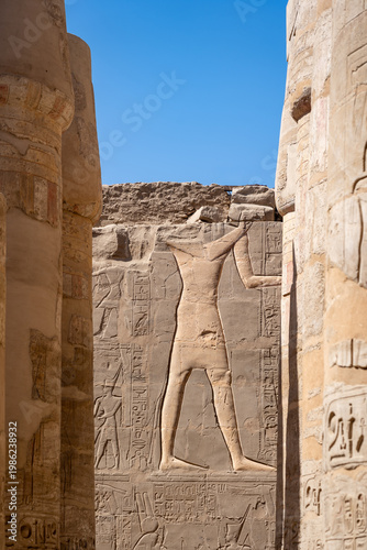 ancient egyptian wall reliefs and hieroglyphs at the karnak temple complex in luxor egypt showing a large pharaoh figure and ancient architectural ruins