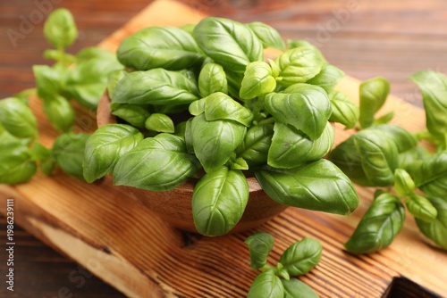 Fresh basil leaves and bowl on wooden table, closeup