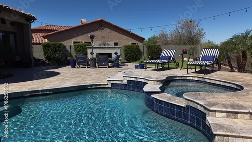 A 4k aerial view of a desert landscaped home in Arizona featuring a travertine tiled pool deck with a fireplace and outdoor kitchen.