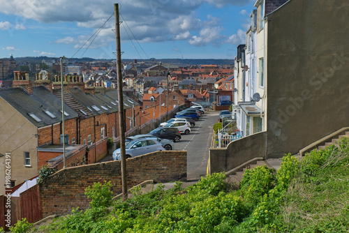 Fotografia A street descends a hill, flanked by houses and parked cars
