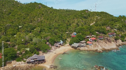 Rocky Shoreline Dotted With Wooden Structures. Turquoise Bay With Small Boats And Clustered Huts