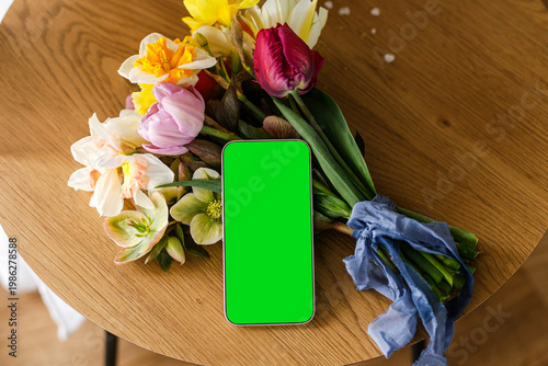 Happy Mother's day! Blank phone screen on beautiful bouquet and gift on wooden table, view above. Phone template. Digital greeting mockup with space for text. International women's day.