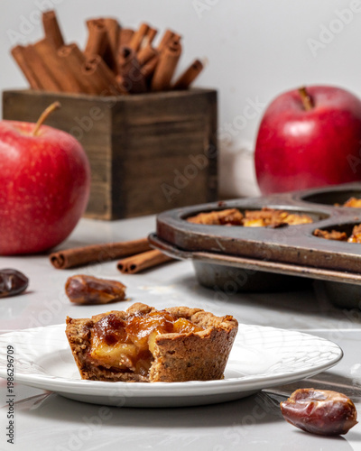 A mini apple pie tart with a bite out and ingredients in behind.