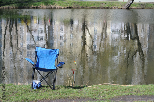 Fishing chair on the bank of a lake with reflection in water.