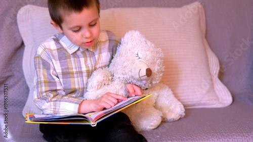 Young Boy Reading Colourful Picture Book on Sofa with Teddy Bear — Early Childhood Literacy Home Learning and Bedtime Reading Concept