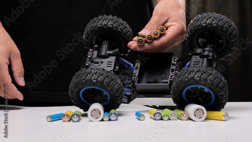 Hand holding batteries over a toy remote control car, with various batteries on a white table