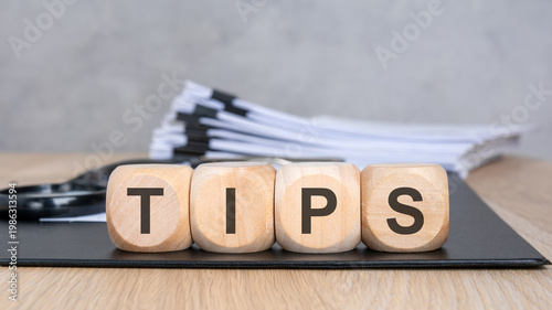 TIPS word on wooden blocks. Blurred background with a document stack and magnifying glass. Business advice and consulting concept.