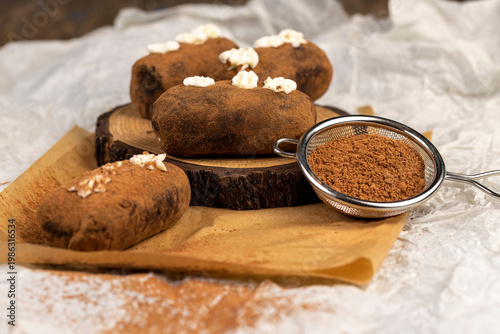 sweet brown pastry potatoes are lying on a serving board and paper, sweet classic cake from butter and a large amount of cocoa mixed with sponge cake and cognac, cocoa powder is scattered nearby