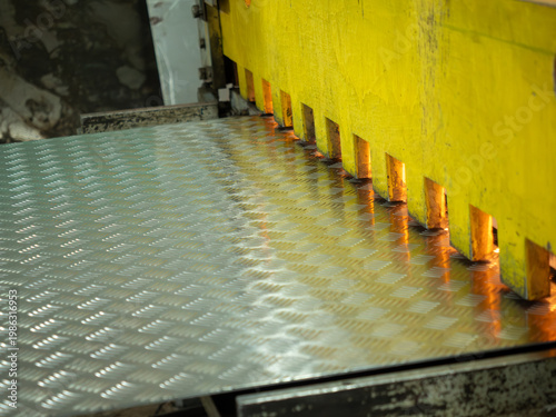 Quadro su tela Heavy duty guillotine shears with yellow protective guard press down on silver diamond plate steel during precise industrial manufacturing cutting process in professional metalwork factory workshop