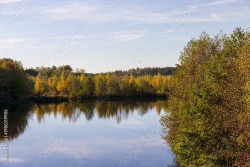 autumn lake in sunny weather at sunset, beautiful deciduous trees on the riverbank before the fall of leaves, evening before sunset