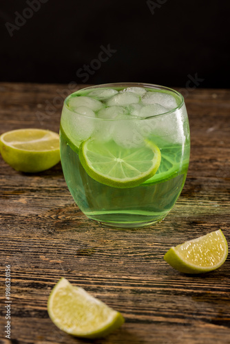 one cold lime-flavored carbonated drink with lots of gas bubbles and whole pieces of fresh sour lime, sweet green-colored carbonated drink poured into a glass with ice