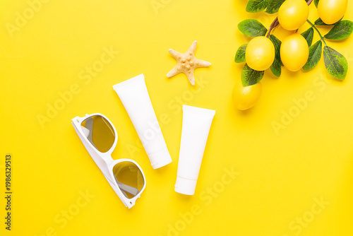 Two unbranded white tubes with skin care products such as cream, balm, lotion, shampoo or serum with citrus extract and vitamin C on bright yellow background decorated with lemon branches top view. 