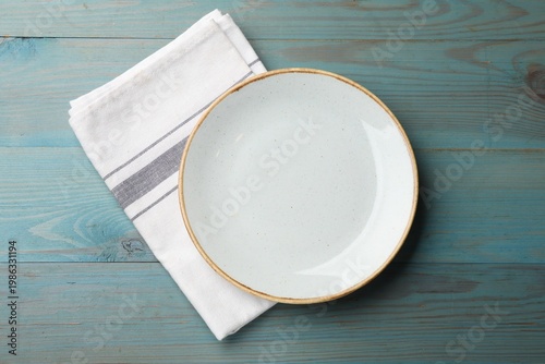 Empty plate and napkin on light blue wooden table, top view