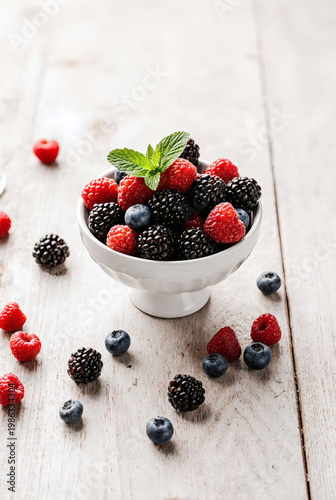 Fresh berries in a white bowl on a wooden table with some scattered around during daytime