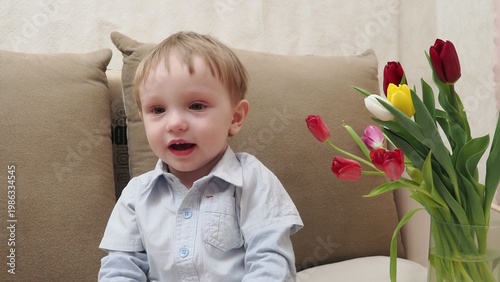 Beautiful young boy with tulips flowers and gift box. A gift for mom in a small red box from her son. Happy Mother's Day