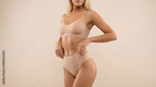 A clean studio shot of a young blonde tanned woman in minimal inner wear