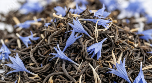 Close up view of dried tea leaves mixed with blue flowers on a flat surface for herbal tea preparation and enjoyment