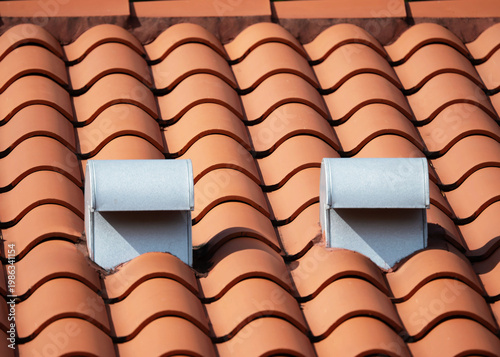 Photography Orange clay barrel tile roof has an attached attic ventilation system comprised of steel gooseneck vents