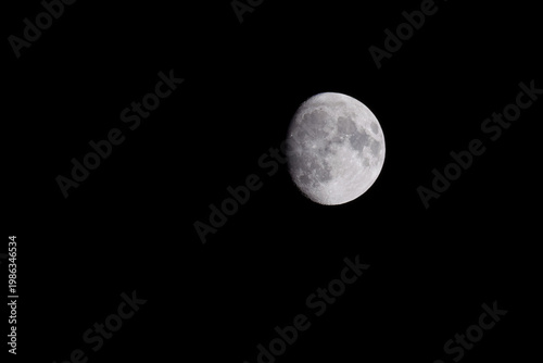 Waxing gibbous moon on black night sky, detailed lunar surface visible in dark minimal space background